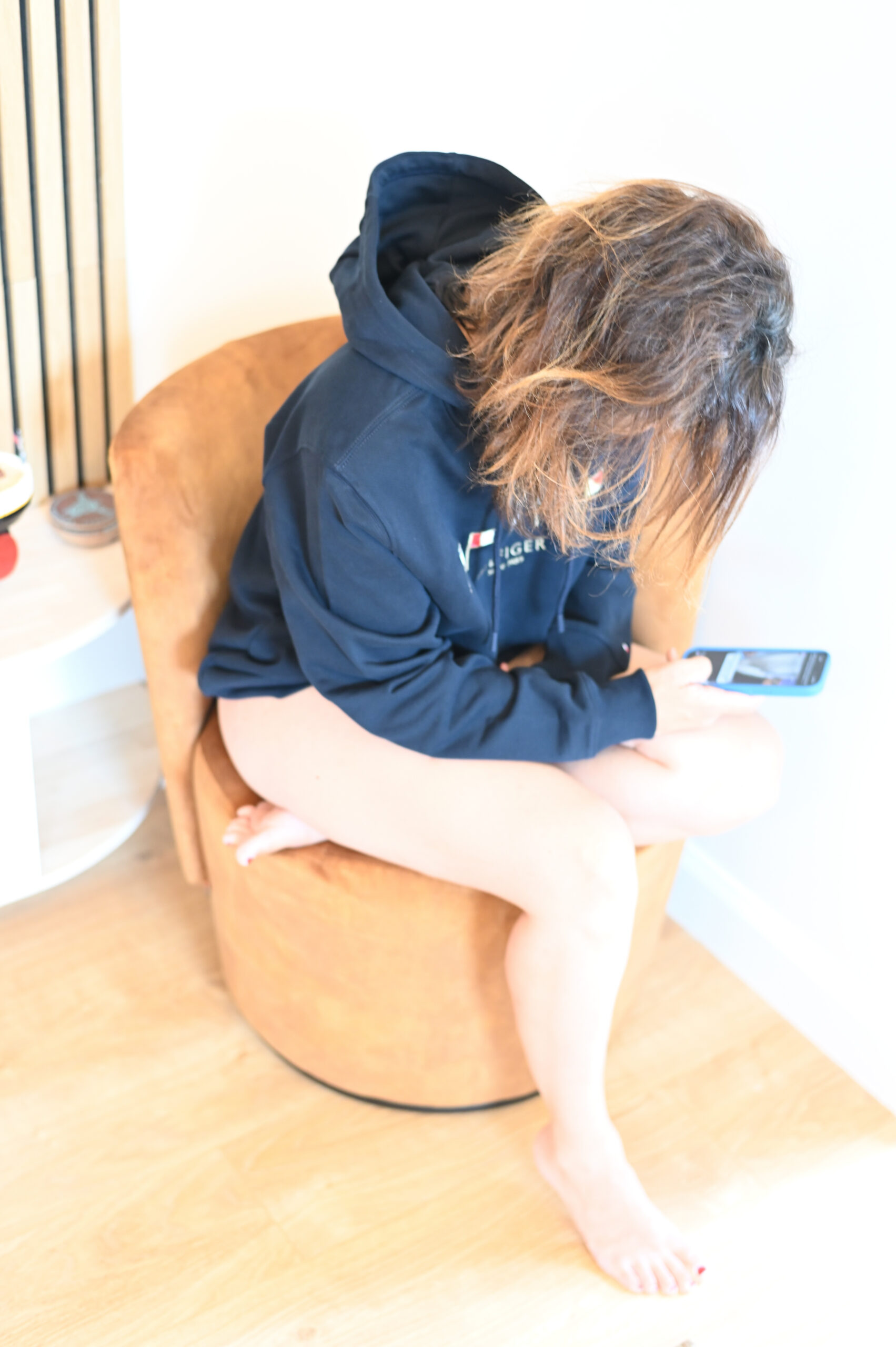 Kvinna i marinblå hoodie sitter avslappnat på golvet med telefon bredvid sig