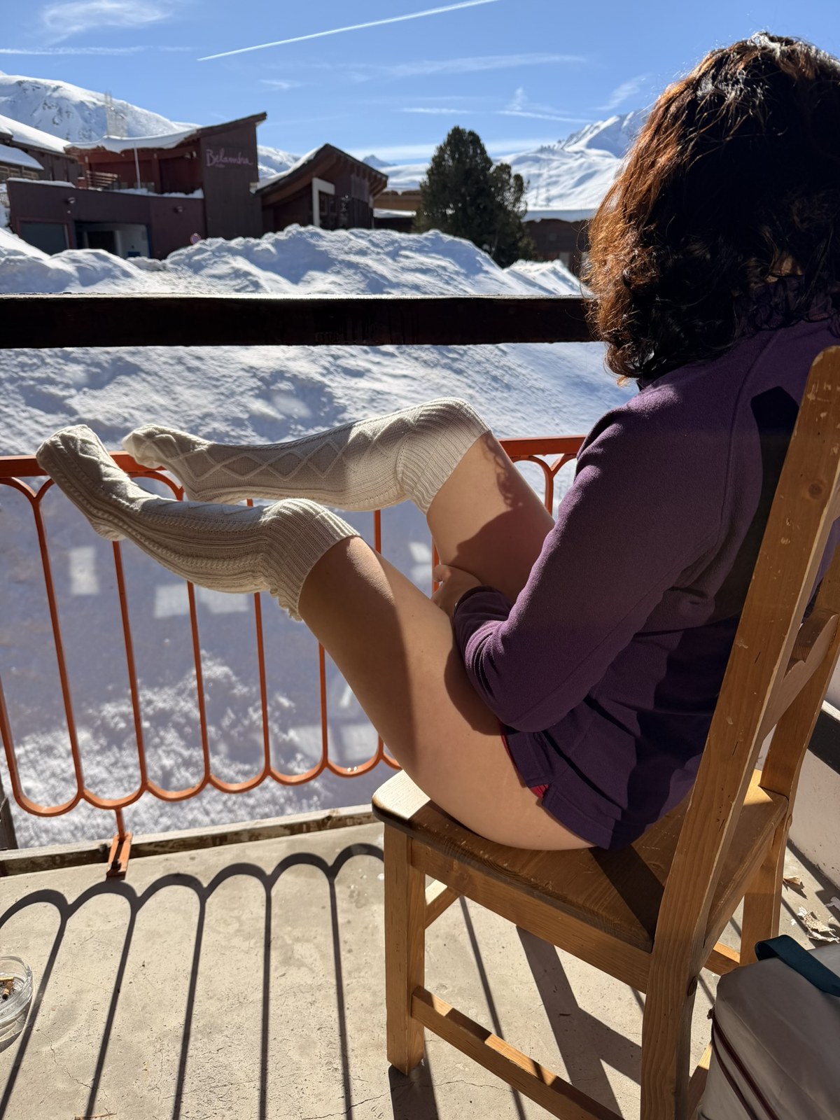 Klara sitter på en snöig terrass i yllesockor och stickad tröja, med snödrivor i bakgrunden